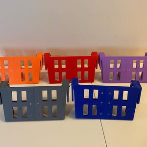 May include: Five colorful, rectangular storage baskets in orange, red, purple, gray, and blue. Each basket has a series of rectangular cutouts and a handle on each side. The baskets are arranged on a white surface.