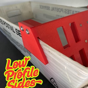 May include: A red plastic bracket with a rectangular design is attached to a white box. The box has text that reads "UNITED STATES POSTAL SERVICE". The image also contains the text "Low Profile Sides" in a yellow and red font.