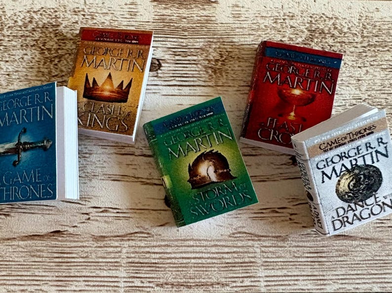 K&ouml;nnte beinhalten: Miniatur-Buchset mit Titeln von George R.R. Martin, darunter "Game of Thrones", "Clash of Kings", "Storm of Swords", "Feast for Crows" und "Dance with Dragons". Die B&uuml;cher haben farbenfrohe Einb&auml;nde und wei&szlig;e Seiten.