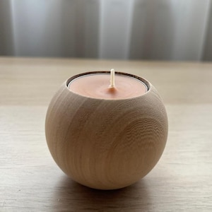 Op de afbeelding: Een ronde houten kaarsenhouder met een natuurlijke houten afwerking. Een kleine theelichtkaars is in de houder geplaatst.