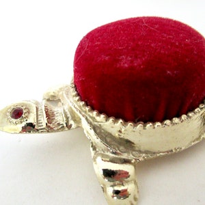 May include: A silver turtle pincushion with a red velvet top and a single red jewel on the head.