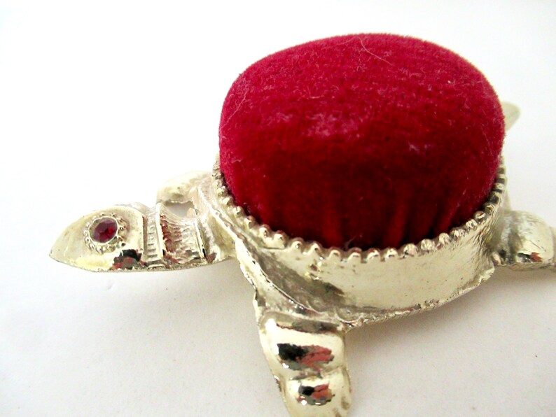 May include: A silver turtle pincushion with a red velvet top and a single red jewel on the head.