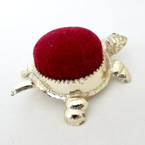 May include: A silver turtle pincushion with a red velvet top. The turtle has a detailed shell and four legs.