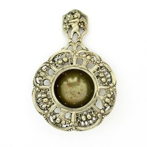 May include: Silver tea strainer with a decorative design featuring a cherub and floral motifs. The strainer has a round, perforated base and a handle with a loop at the top.