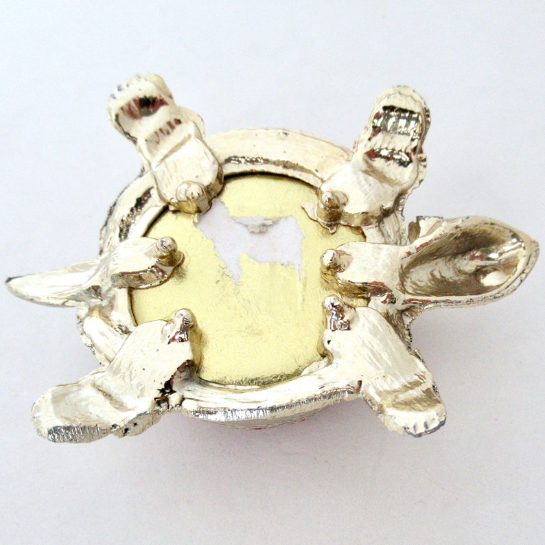 May include: A silver turtle trinket box with a round, gold-colored interior. The turtle has a detailed shell and four legs.