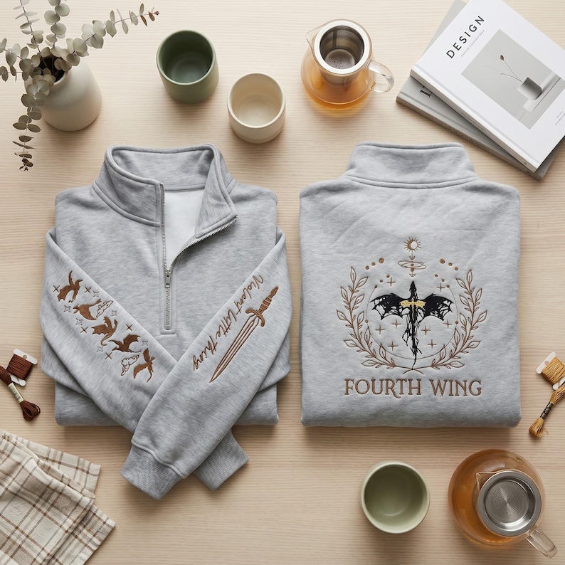 Peut inclure: Deux sweat-shirts gris clair &agrave; fermeture &eacute;clair quart de zip. L'un pr&eacute;sente des dragons brod&eacute;s et le texte "Violent Little Thing" sur la manche, ainsi qu'une &eacute;p&eacute;e. L'autre a un motif circulaire avec une cr&eacute;ature ail&eacute;e et le texte "FOURTH WING".