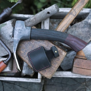 Puede incluir: Una herramienta de talla forjada a mano con mango de madera y funda de cuero. La herramienta tiene una hoja curva y un logotipo de corona en la cabeza de metal. El texto "Enjoy the Carving" es visible en el fondo.