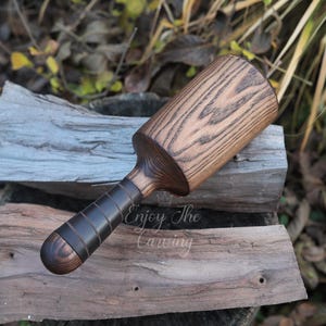 May include: A wooden mallet with a cylindrical head featuring a prominent dark brown wood grain pattern and a smooth, dark brown handle with a series of horizontal grooves. The text Enjoy The Carving is visible on the mallet head.