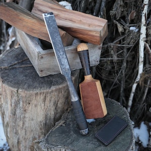 May include: Two woodworking tools on a tree stump. A long, black metal chisel with a wooden handle and a wooden mallet with a brown leather striking surface.
