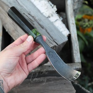 以下が含まれることがあります： 暗い柄と湾曲した銀色の刃が付いた彫刻ツール。 ハンドルには刃の近くに緑色のアクセントがあります。 画像には「Enjoy The Carving」というテキストが表示されています。 このツールは、木工や彫刻用に設計されているようです。