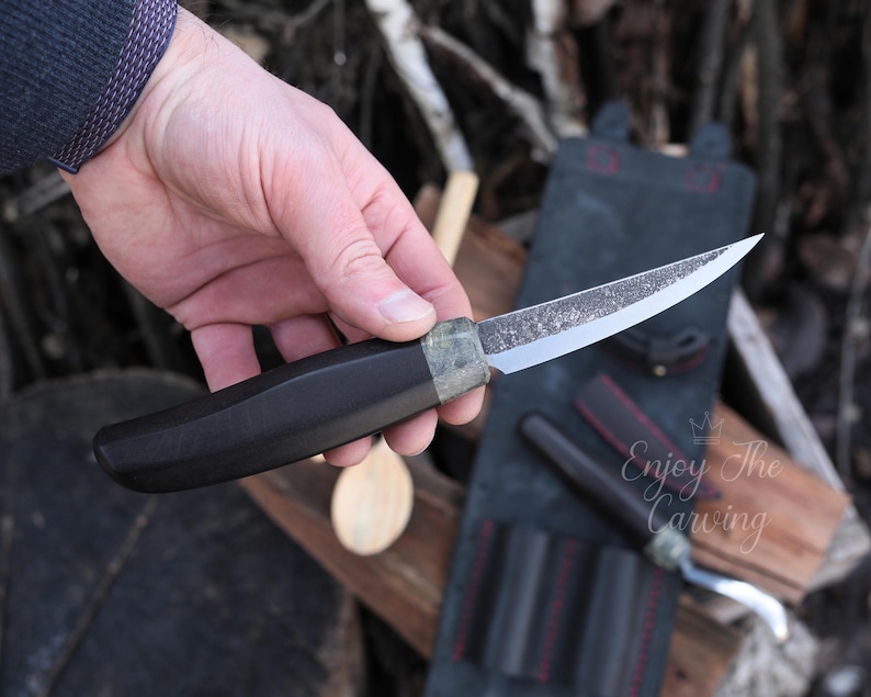 K&ouml;nnte beinhalten: Ein Messer mit schwarzem Griff, einer gebogenen Klinge und einer strukturierten Oberfl&auml;che. Das Messer wird in der Hand gehalten und die Klinge ist scharf. Das Messer ist Teil eines Sets von Schnitzwerkzeugen.