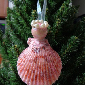 May include: A pink seashell ornament with a pearl trim, hanging on a Christmas tree.