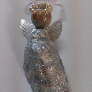 May include: A silver glitter angel ornament with a pearl crown and wire wings. The angel is made from an oyster shell.