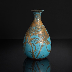 May include: A ceramic vase with a bulbous body and a narrow neck, featuring a vibrant turquoise blue base glaze overlaid with a textured, metallic bronze-colored pattern that resembles organic, branching shapes or abstract, flowing lines.