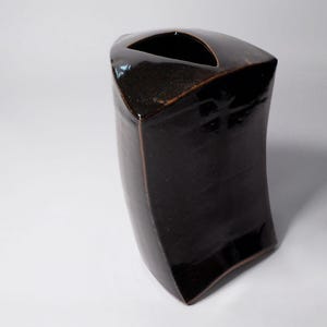 Może przedstawiać: Brązowy ceramiczny wazon o unikalnym, kanciastym wzorze. Wazon ma szeroki otwór u góry i wąską podstawę.