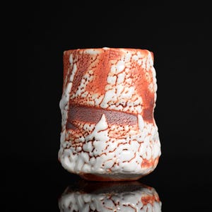 May include: A cylindrical ceramic cup featuring a textured surface with a combination of deep terracotta red and thick, raised white glaze. The exterior displays a crackled, uneven finish with organic patterns where the white glaze drips.