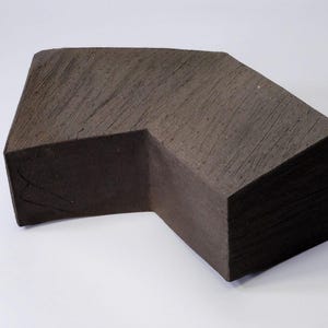 Puede incluir: Una escultura de cerámica de color marrón oscuro con una forma geométrica. La escultura tiene una superficie rugosa y texturizada y parece estar hecha de arcilla.
