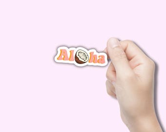 May include: A sticker with the word "Aloha" in pink letters with a yellow outline, and a coconut illustration. The sticker is held by a hand against a light pink background.
