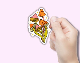 Può includere: Un adesivo colorato con un gruppo di funghi stilizzati. I funghi hanno cappelli arancioni e rosa con branchie e gambi gialli. Il design include accenti di stelle gialle, creando un'estetica stravagante ispirata alla natura.