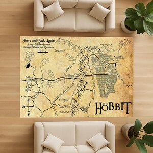 May include: A large, rectangular rug featuring a map from "The Hobbit." The map is in sepia tones with black text and illustrations, including the words "The Hobbit." The rug is placed on a wooden floor, with two cream-colored sofas and plants.