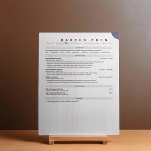 May include: A professional resume document for Marcus Chen printed on white paper, featuring sections for summary, experience, education, and awards. The text is black, organized in a clean layout, and displayed on a small wooden stand.