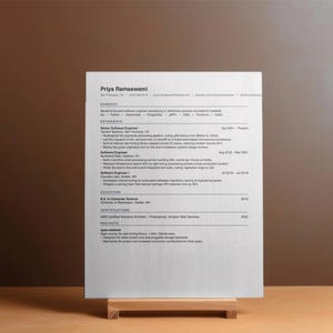 May include: A white printed resume for Priya Ramaswami displayed on a small wooden stand. The document includes sections for summary, experience, education, certifications, and projects, detailing a career as a software engineer in San Francisco.