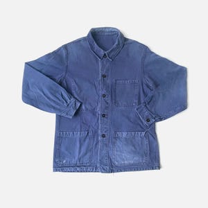 May include: A blue work jacket with four front pockets, two chest pockets, and button closures. The jacket has long sleeves and a collared neckline. The fabric appears to be a durable cotton or similar material, with a slightly faded appearance.
