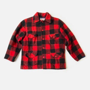 May include: A red and black plaid jacket with four front pockets and a button-down closure. The jacket has long sleeves and a collared neckline. The fabric appears to be a thick wool or wool blend.