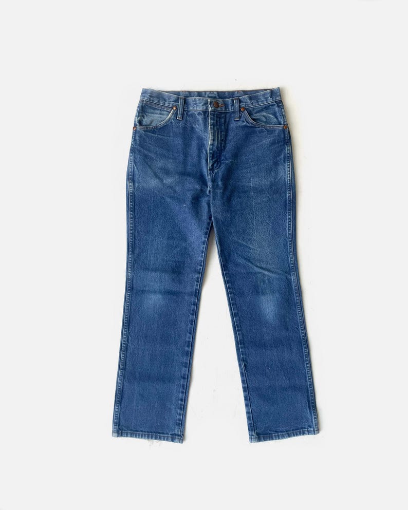 May include: A pair of blue denim jeans with a classic five-pocket design. The jeans have a straight leg cut and a button and zip closure. The denim has a faded appearance, suggesting wear. The jeans are displayed on a white background.