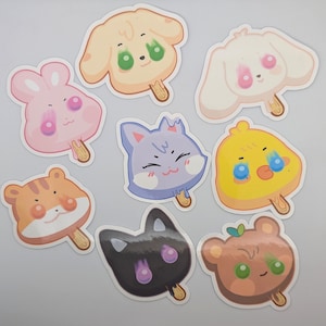 May include: A collection of eight cartoon animal-shaped stickers resembling popsicles. The stickers feature a variety of animals, including a dog, bunny, cat, chick, tiger, and bear, in pastel colors with cute expressions.