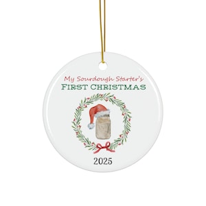 May include: White ceramic Christmas bauble featuring a green wreath, red bow, and a glass jar with a red Santa hat. The text reads "My Sourdough Starter's First Christmas 2025".