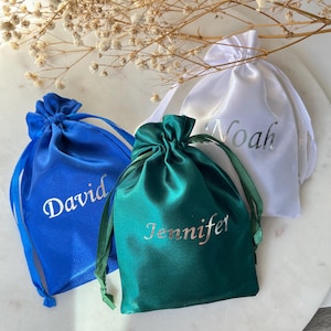 May include: Three satin drawstring bags in white, blue, and green with the names Noah, David, and Jennifer embroidered in silver on the front.