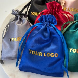 May include: Assortment of colorful satin drawstring bags with gold lettering that reads "YOUR LOGO".