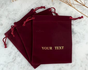 May include: Set of four burgundy velvet drawstring pouches with gold embroidery. The pouch in the front has the text "YOUR TEXT" embroidered on it.