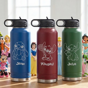 Puede incluir: Tres botellas de agua aisladas en azul, burdeos y verde, cada una con una tapa negra. Las botellas presentan un contorno blanco del personaje Stitch de Lilo & Stitch, con nombres debajo. Figuras de Disney en el fondo.