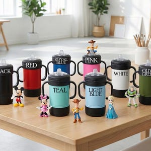 Puede incluir: Una colecci&oacute;n de vasos con boquilla aislados de colores en negro, rojo, azul real, rosa, blanco, verde oliva, turquesa y azul claro. Cada vaso tiene un asa negra y una figura de personaje.
