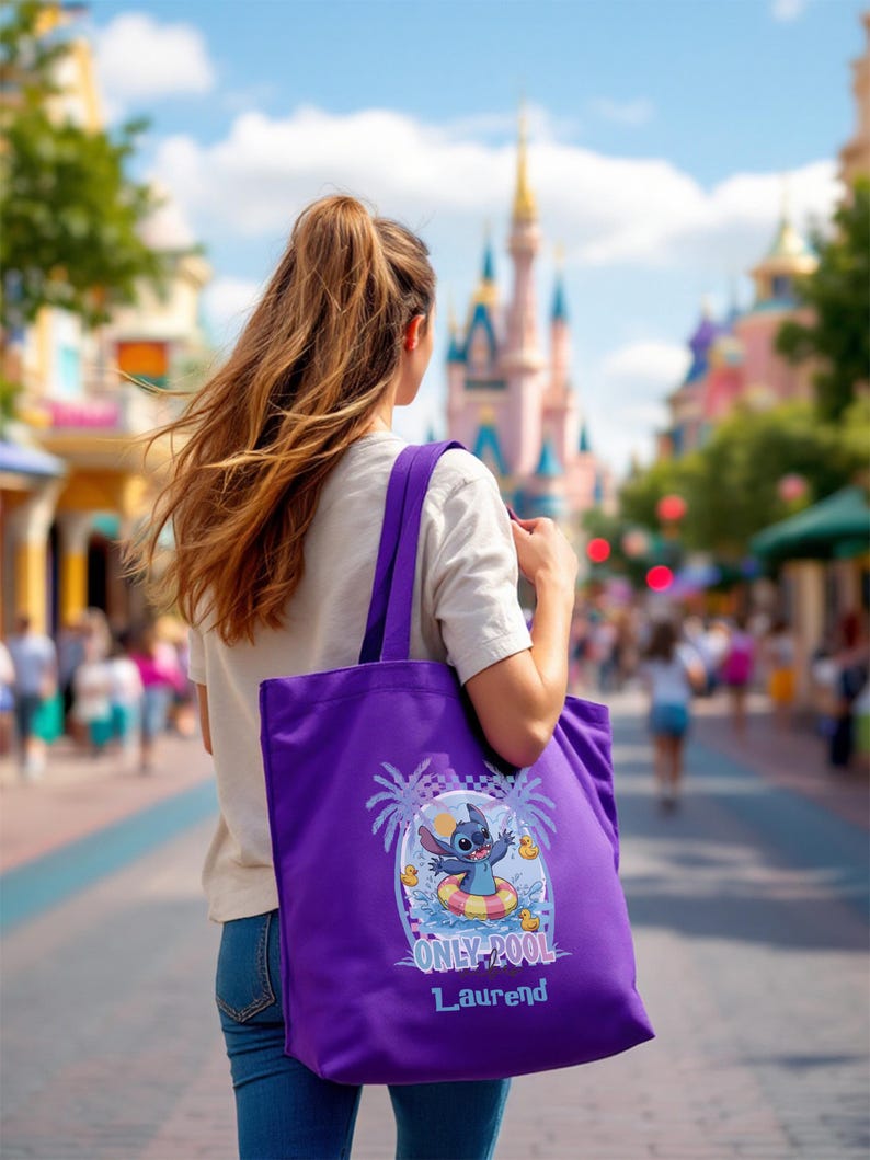 May include: A purple tote bag featuring a cartoon character in a pool floatie with the text "ONLY COOL" and a name. The bag is carried by a person walking down a street with a castle in the background.