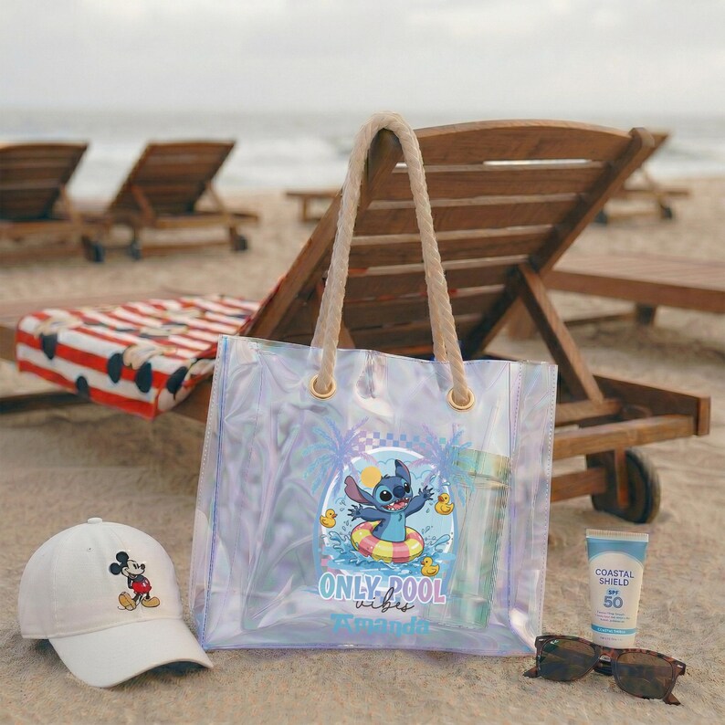 May include: A clear tote bag with rope handles featuring a Stitch graphic, a white baseball cap with a Mickey Mouse design, sunglasses, and sunscreen on a sandy beach. The bag has the text "ONLY pool vibes".