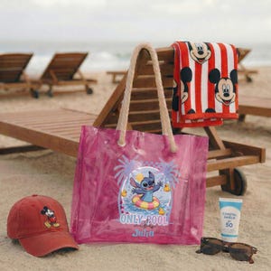 May include: A beach-themed collection featuring a red baseball cap with a Mickey Mouse graphic, a clear pink tote bag with a Stitch design, a red and white striped towel with Mickey Mouse faces, sunglasses, and sunscreen.