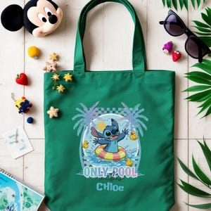 May include: A green tote bag featuring a cartoon Stitch character in a pool float with the text "ONLY POOL vibes" and the name "Chloe". The bag is surrounded by decorative elements including a Mickey Mouse plush, sunglasses, and tropical leaves.