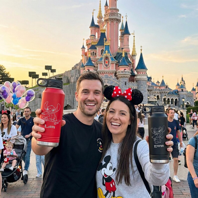Puede incluir: Una botella de agua roja con tapa negra y un dise&ntilde;o de Stitch, sostenida por una persona. La botella tiene grabado el nombre "Liam". Otra persona sostiene una botella de agua negra con un dise&ntilde;o de Stitch y el nombre "Emma".