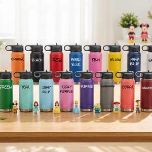 Puede incluir: Una colecci&oacute;n de botellas de agua aisladas de colores vibrantes, incluyendo naranja, negro, rojo y verde. Cada botella tiene una tapa negra y una etiqueta con un nombre de color a juego. Las botellas est&aacute;n dispuestas sobre una superficie de madera.