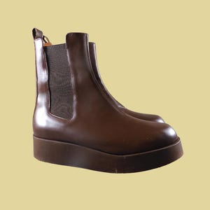 May include: A pair of brown Chelsea boots with a platform sole. The boots have a polished leather finish and elastic side panels. The platform sole adds height and a modern touch to the classic boot design.