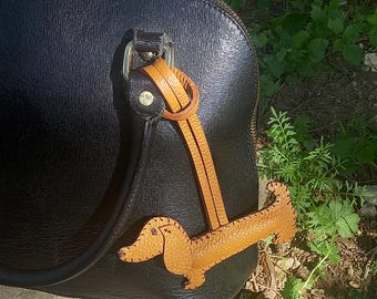 May include: A black leather handbag with a brown leather dachshund keychain. The dachshund is a popular breed of dog known for its long body and short legs.