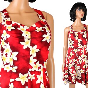 Puede incluir: Un vestido rojo sin mangas con estampado floral blanco. El vestido tiene un escote de corazón y un corpiño ajustado. La falda es amplia y fluida.