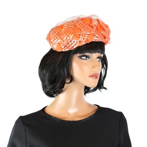 May include: A bright orange woven hat with a net veil. The hat is made of a soft, pliable material and has a rounded shape.