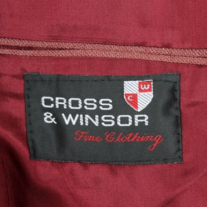 May include: A black label with white text that reads "CROSS & WINSOR Fine Clothing". A red and white crest with a "C" and a "W" is above the text.