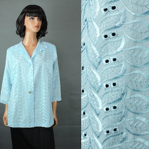 May include: A light blue, button-down blouse with three-quarter sleeves. The blouse features intricate eyelet embroidery and a scalloped hem. The fabric has a leaf-like pattern. The blouse is displayed on a mannequin.