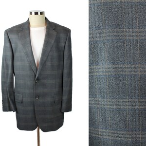 May include: A charcoal gray blazer featuring a subtle windowpane plaid pattern in muted blue and tan lines. The jacket includes a notched lapel, two front buttons, and two flap pockets, displayed on a mannequin over a plain white t-shirt.