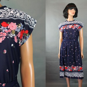 May include: A navy blue midi dress with a floral print featuring red, pink, and white flowers. The dress has a white lace trim at the neckline and hem. The dress has short sleeves and a tie belt at the waist.